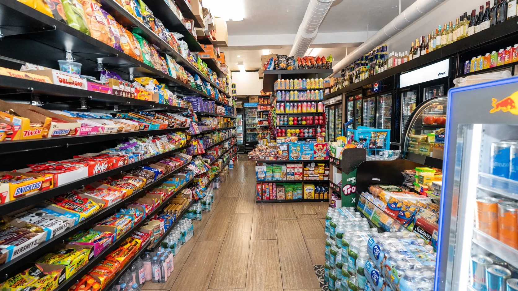 The main aisle inside WYN MKT, with snack shelves, drink coolers and bottled water