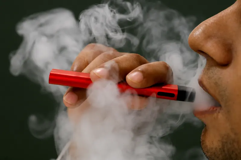 Adult exhaling vapor from a red disposable vape